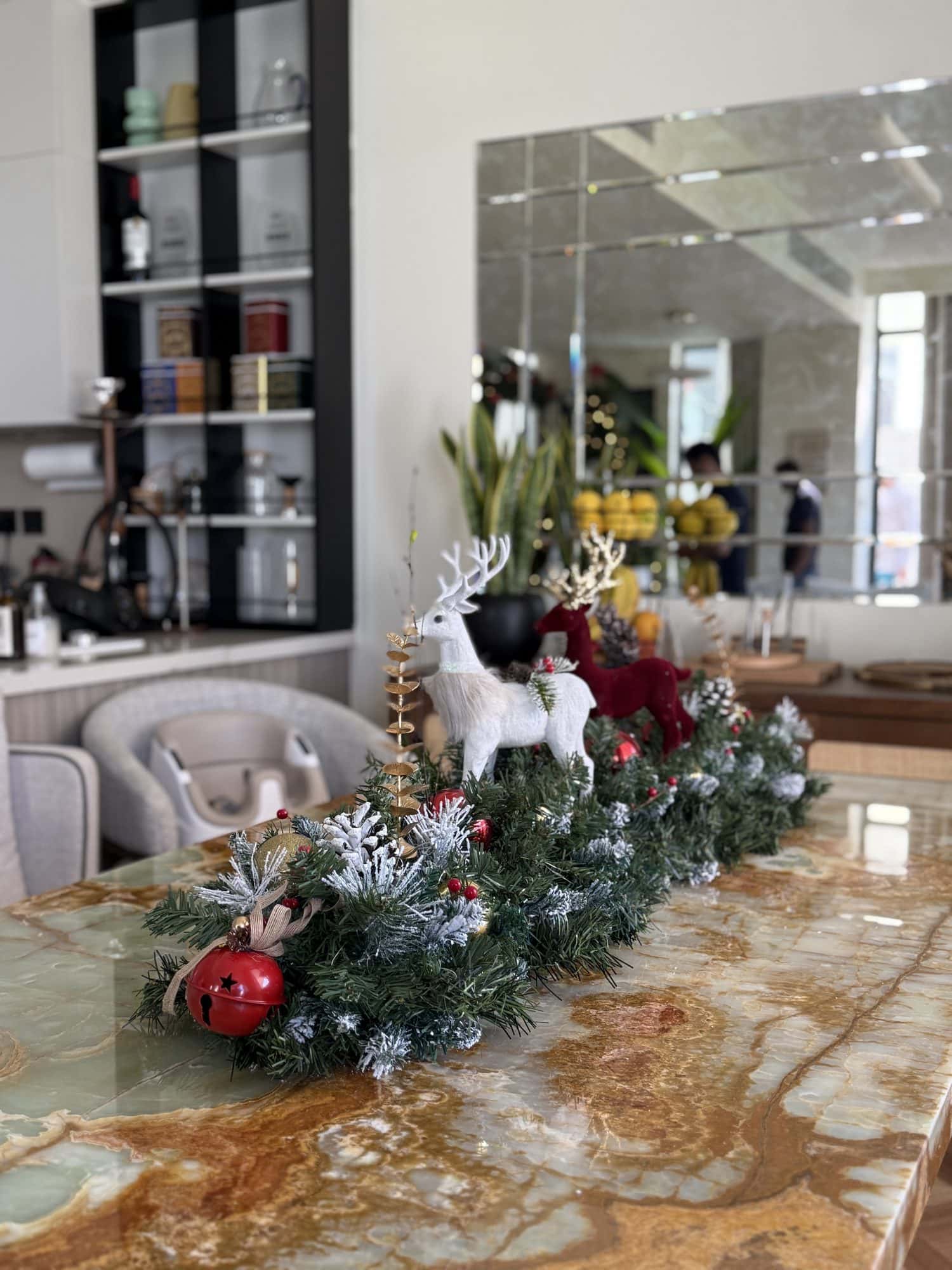 Frosted evergreen runner along an onyx marble counter with a white reindeer, a burgundy reindeer and a red jingle bell