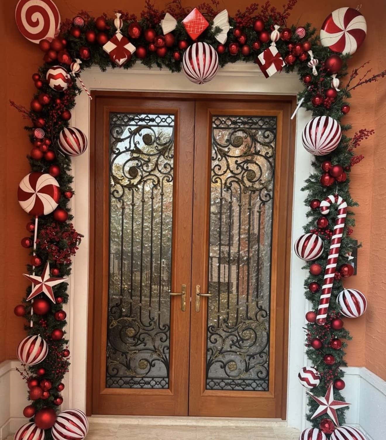 Wrought-iron double doors framed by a playful arch of peppermint swirls, candy canes, stars and red and white striped baubles