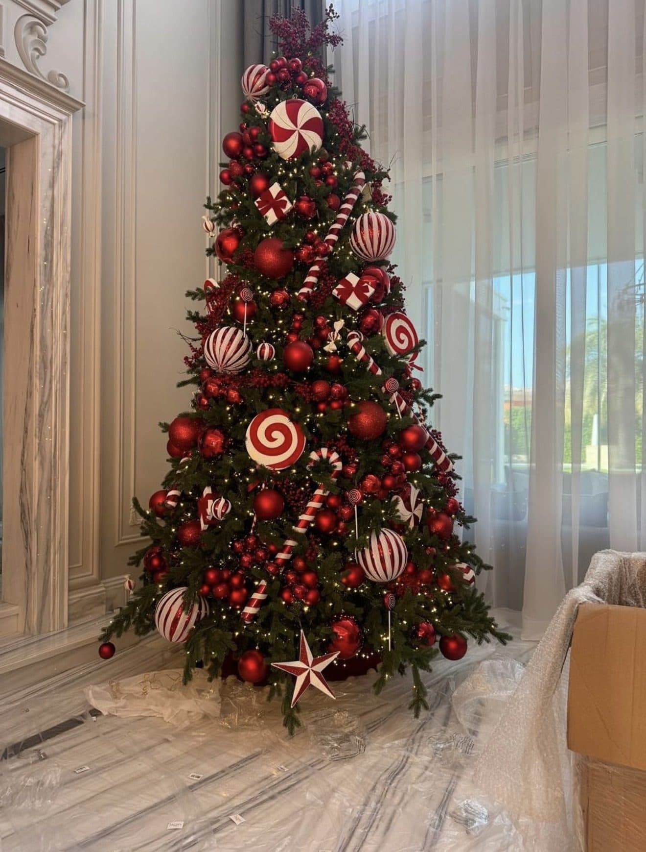 Christmas tree with peppermint and red ornaments part-way through installation, standing on protective sheeting in a marble room